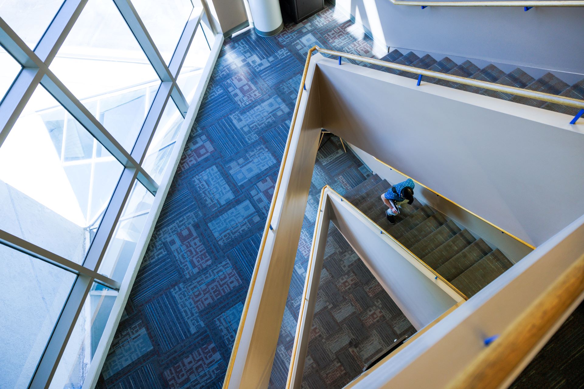 Staircase inside a modern university building with geometric windows and patterned carpets, showing a person descending the stairs